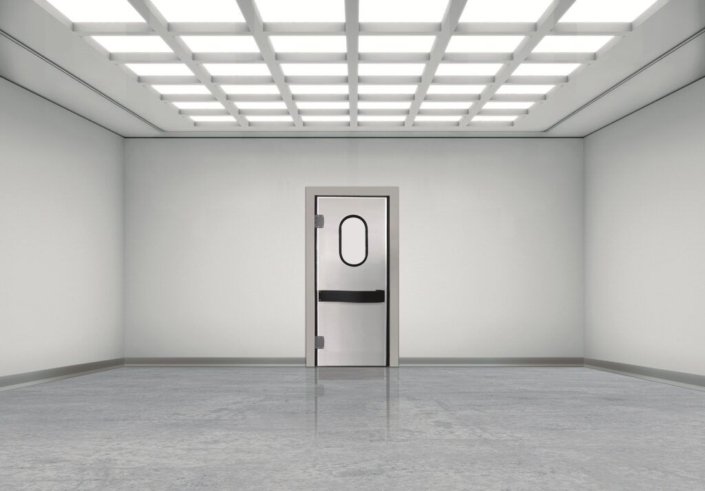 Empty gray room with metal door and oval window under grid lights.