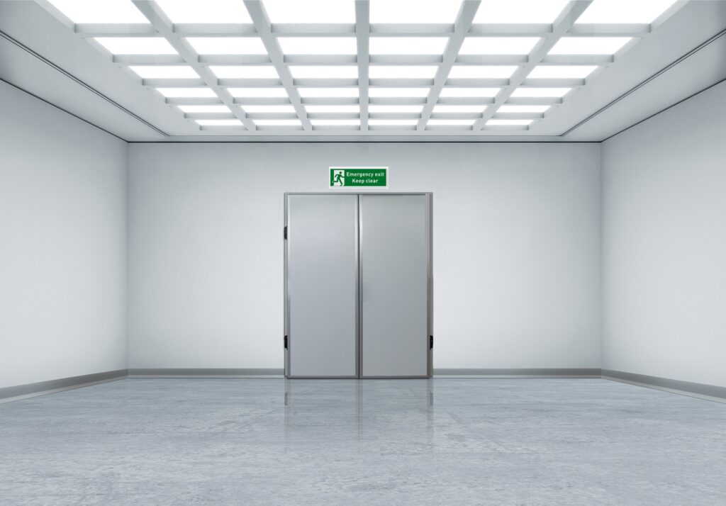 Empty white corridor with double gray doors and an emergency exit sign.