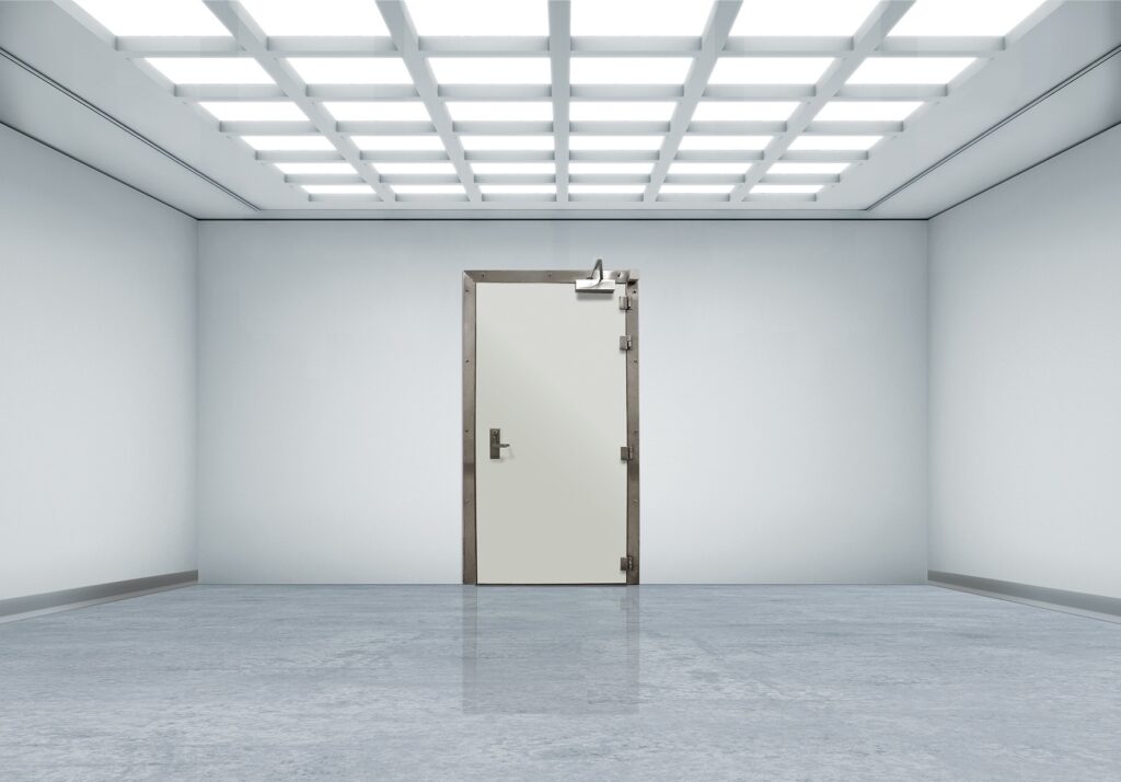 Stainless-framed door centered in a bright, sterile white room with reflective floor